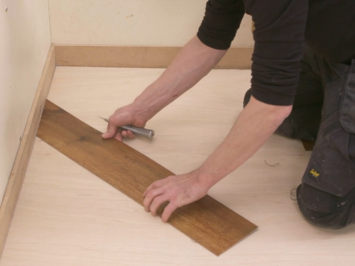 Installer fitting a gluedown plank at a 45 degree angle to the wall